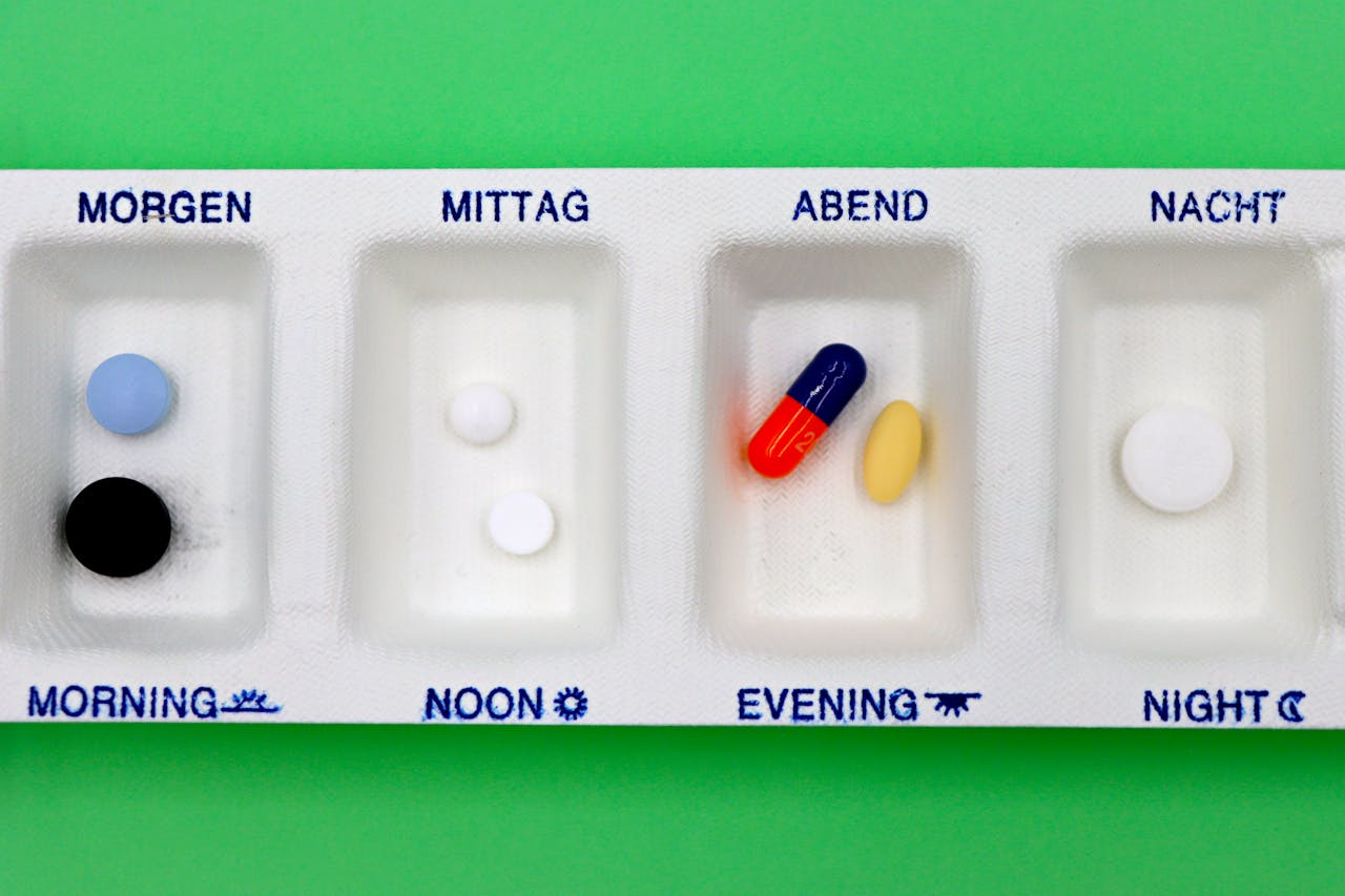 A daily medication organizer with pills for different times, set against a green backdrop.