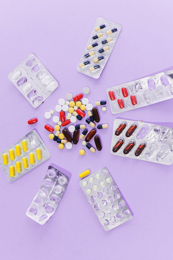 A flat lay of various pills and blister packs arranged on a purple surface, showcasing medication diversity.